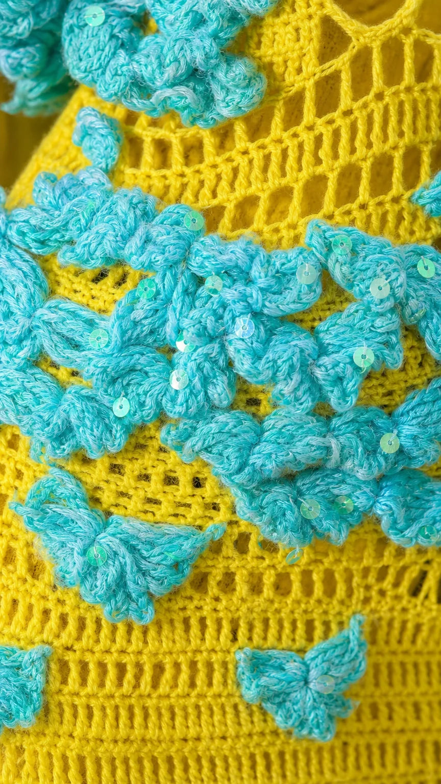 Close-up detail of turquoise 3D floral crochet appliques with clear sequins on yellow knit fabric